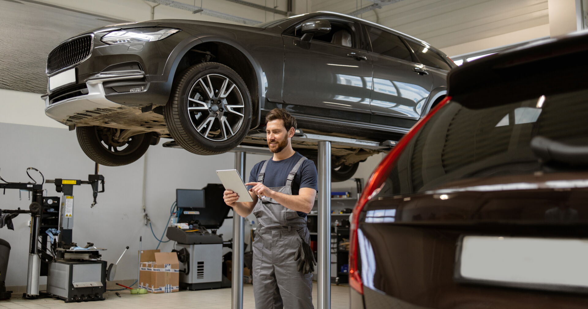Fahrzeugdiagnose mit Tablet in Vetschau | Reifendienst Böhme Ein Mechaniker mit Tablet unter einem aufgebockten grauen SUV in einer Werkstatt. Reifendienst Böhme in Vetschau bietet moderne Fahrzeugdiagnose.